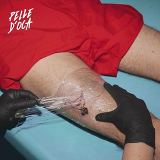 A leg being tattooed, wrapped in cling film, held by black-gloved hands on a teal surface.