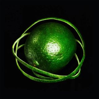 A lime with its peel spiraling around it like orbital rings, against a black background.