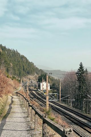 On the left a hiking trail leading towards a forrest, right next to it three train tracks next to each other and a bit bag a white house next to the tracks