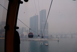 A view from a cable car overlooking a city skyline and a bridge across a foggy bay, with other cable cars visible.