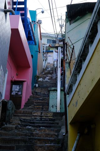 A narrow, winding stairway ascends between colorful, weathered buildings in a bustling alleyway.