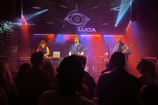 Artur the Gang at Lucia, singer with guitar center stage, keyboardist on the left, bassist on the right, red and blue haze over the crowd.